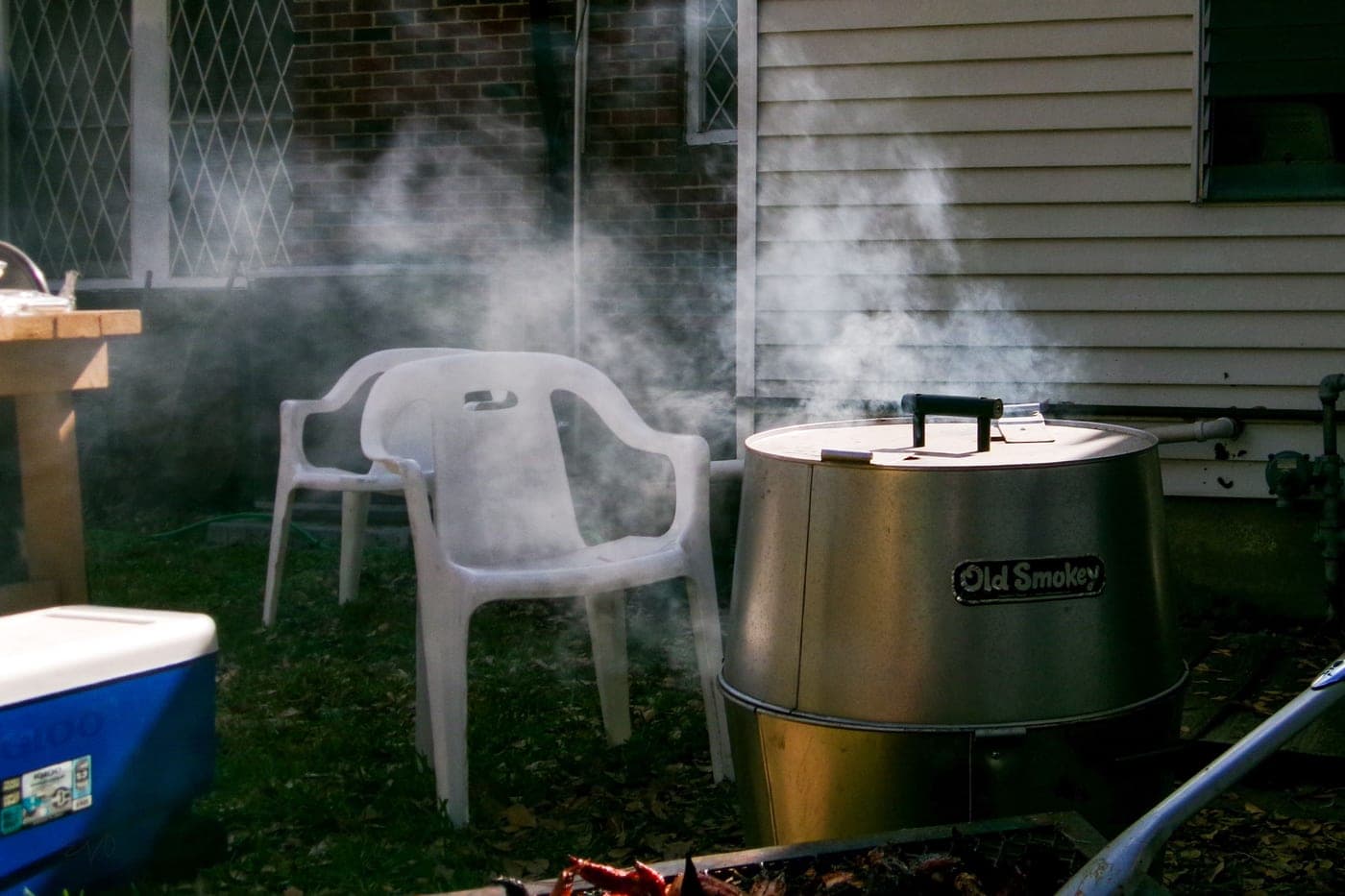Smoke rising from a barrel offset smoker in a backyard